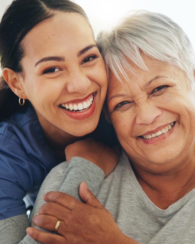 Home health aid hugging older woman from behind